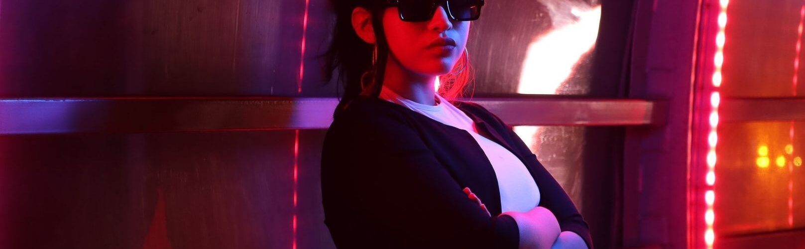 Person mit Sonnenbrille und dunkler Kleidung im farbig beleuchteten Club