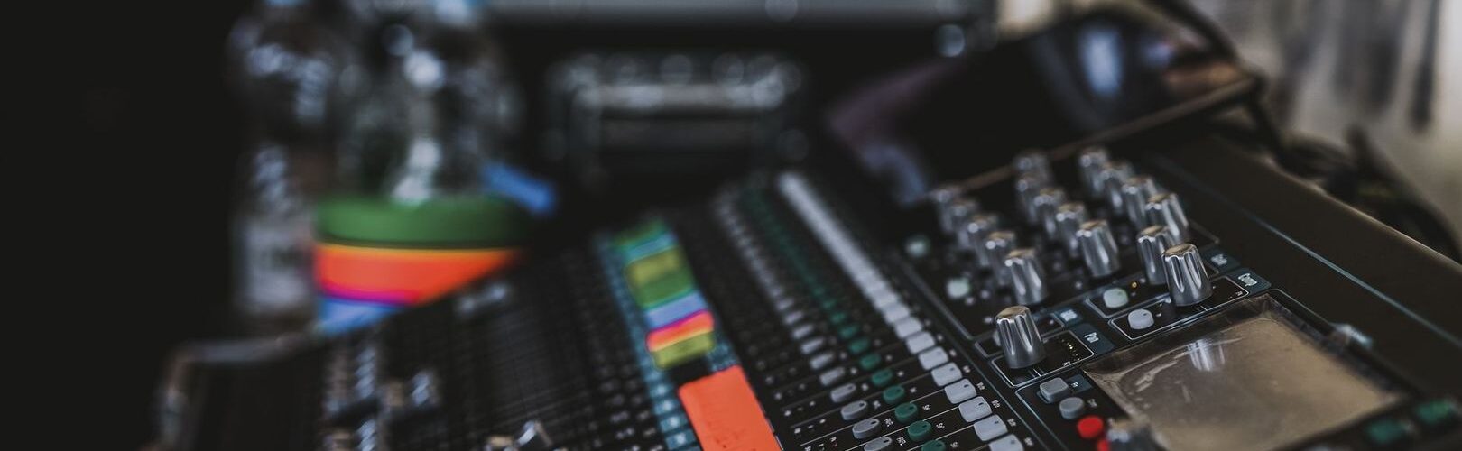 Nahaufnahme eines Audiomischpults mit Reglern und farbigen Pegelanzeigen