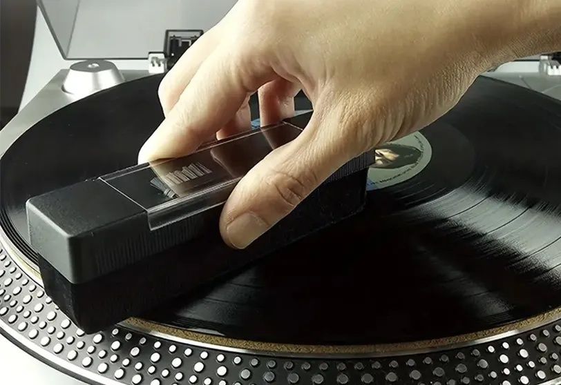 Hand führt eine Reinigungsbürste über eine schwarze Vinylschallplatte